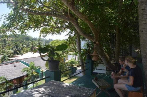 two people sitting on a balcony looking out at the trees at Villa tadini in Galle