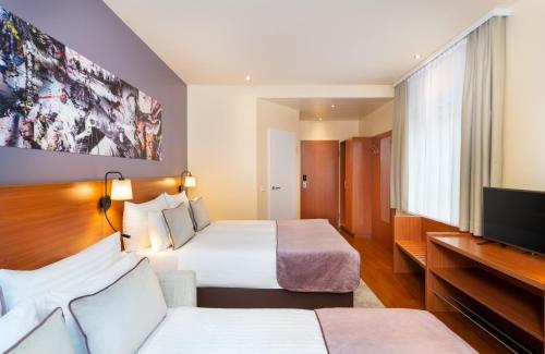 a hotel room with two beds and a flat screen tv at Leonardo Hotel Salzburg City Center in Salzburg