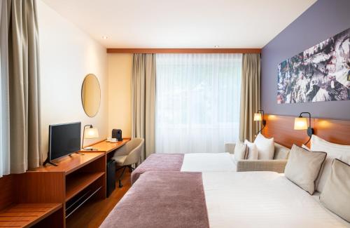 a hotel room with two beds and a desk at Leonardo Hotel Salzburg City Center in Salzburg