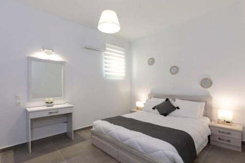 a white bedroom with a bed and a desk and a window at Michaela's Apartment in Koskinou