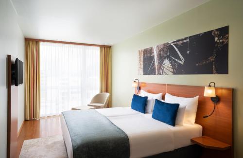 a hotel room with a large bed with blue pillows at Leonardo Hotel Salzburg Airport in Salzburg