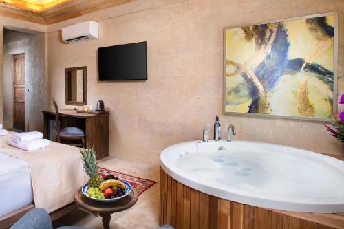 a bathroom with a tub and a bed and a television at Cappadocia Pyramid Stone House in Uchisar