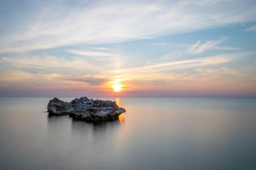 a rock in the water with a sunset in the background at THE VIEW B&B, terrace & more in San Foca