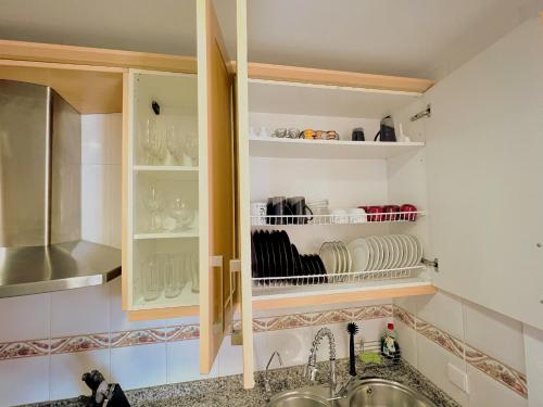 een keuken met een wastafel en een kast met borden bij Beautiful apartment with pools, playground and paddle tennis - Family friendly and near Vithas Hospital - Free parking in garage in Benalmádena