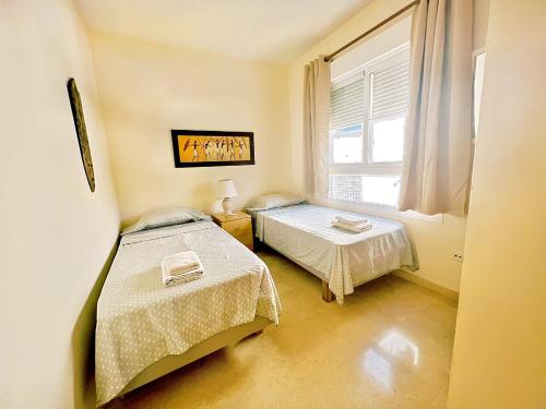 um pequeno quarto com 2 camas e uma janela em Beautiful apartment with pools, playground and paddle tennis - Family friendly and near Vithas Hospital - Free parking in garage em Benalmádena