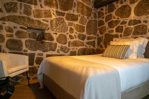 a bedroom with a stone wall with a bed and a chair at Quinta de Silvalde in Santo Tirso