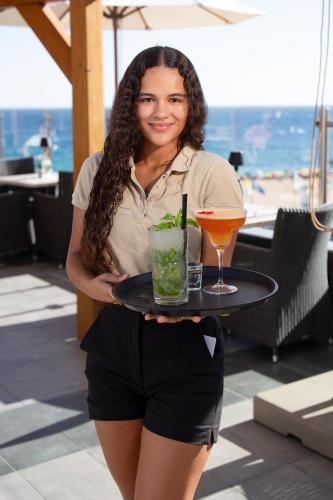 a woman holding a tray with a drink on it at Hotel Carvoeiro Plaza in Carvoeiro
