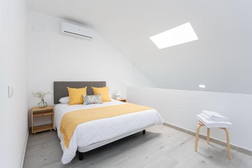 a white bedroom with a bed and a stool at Apartamentos LA PELUSA in Málaga
