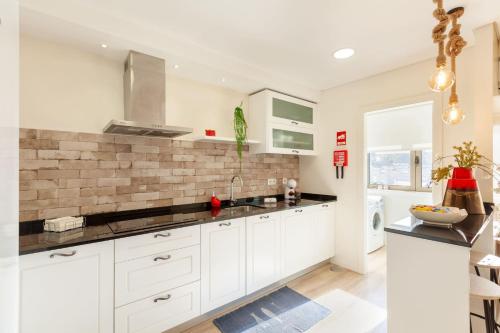 uma cozinha com armários brancos e uma parede de tijolos em Apartamento Lírio - Minho's Guest em Braga