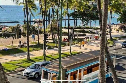 a train on a street with palm trees and the ocean at WELLCOME TO LOVELY CONDO 2 BEDS 2 BATHS FREE PARKING IN WAIKIKI BEACH in Honolulu