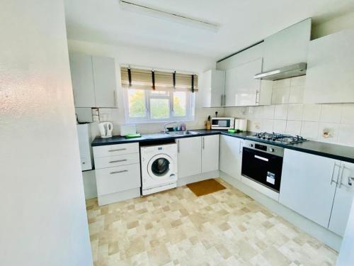 cocina con armarios blancos, lavadora y secadora en Wonderful Apartment in London en The Hyde