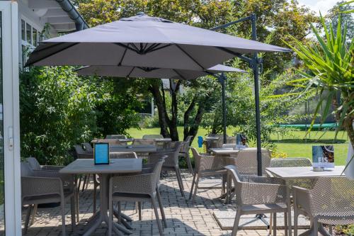 a patio with tables and chairs and an umbrella at Hotel Villa Flora in Velden am Wörthersee