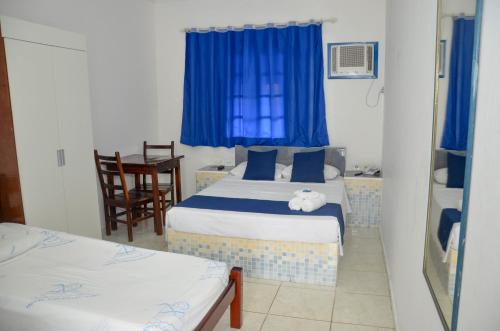 a bedroom with two beds with blue curtains and a table at Hotel Litoral Norte in Caraguatatuba