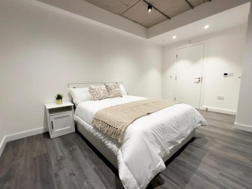 a white bedroom with a bed and a night stand at Stylish Apartment in Greenwich in Abbey Wood