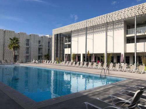 une grande piscine avec des chaises et un bâtiment dans l'établissement Villa moderne Nakara T3 Cabine à Rochelongue, au Cap d'Agde