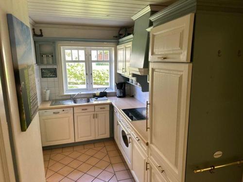 una pequeña cocina con armarios blancos y una ventana en Haus-Deichtraum en Risum-Lindholm