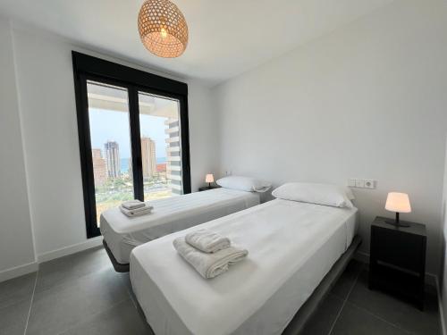 two beds in a white room with a window at Beautiful duplex modern apartment in Calpe - Inmodream Calpe in Ifach