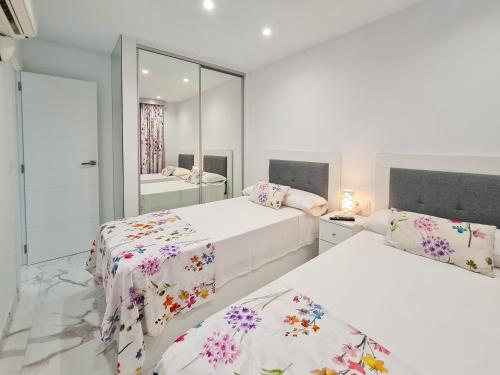 a white bedroom with two beds and a mirror at Apartamento Edificio Astoria in Benidorm