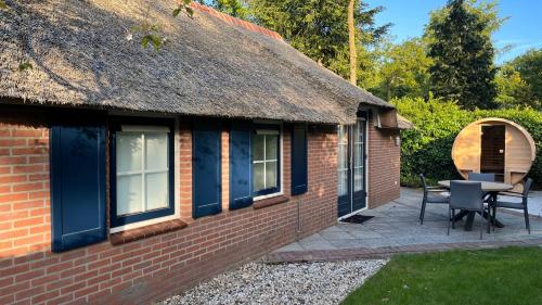 a thatched cottage with a patio and a table and chairs at Villa Victoria with sauna in Ermelo in Ermelo