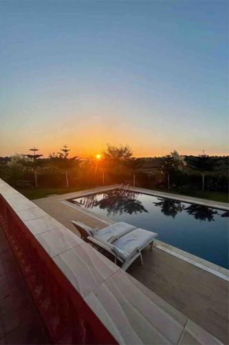 una piscina con 2 tumbonas junto a la puesta de sol en Lovely holiday Private villa with nature view +pool, en Larache