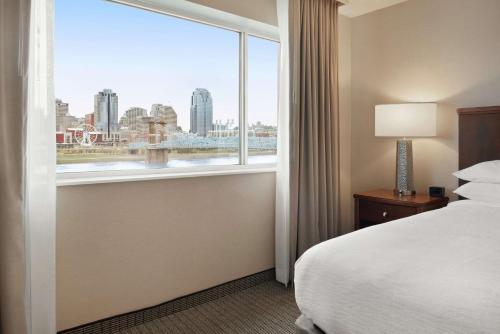 a bedroom with a window with a view of the city at Embassy Suites Cincinnati - RiverCenter in Covington