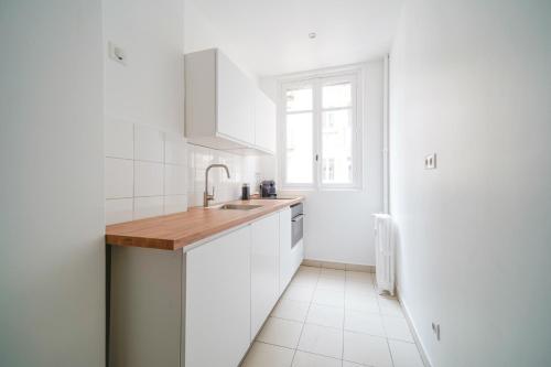 eine Küche mit weißen Schränken, einem Waschbecken und einem Fenster in der Unterkunft Apartment next to Louis Vuitton Fondation in Neuilly-sur-Seine