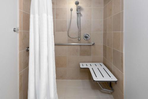 y baño con ducha con cortina de ducha y banco. en Embassy Suites Dallas - Park Central Area, en Dallas