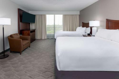 a hotel room with two beds and a chair at Embassy Suites Dallas - Park Central Area in Dallas