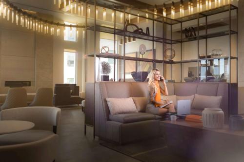 a woman sitting on a couch talking on a cell phone at Canopy By Hilton Dallas Frisco Station in Frisco