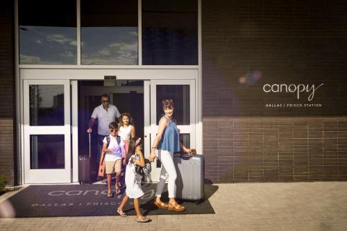 a group of people walking outside of a building with luggage at Canopy By Hilton Dallas Frisco Station in Frisco
