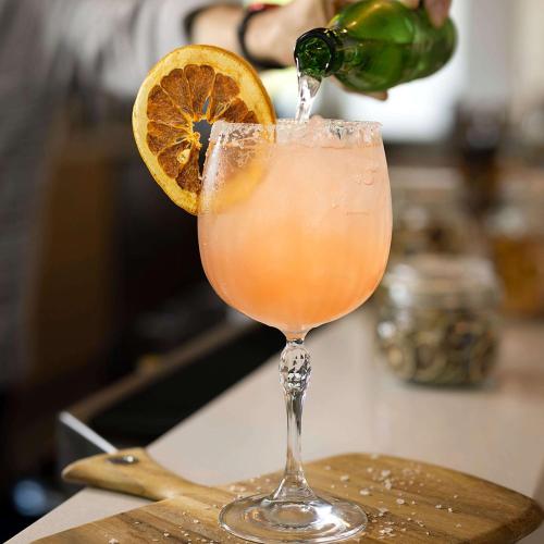 a person pouring a drink into a glass with an orange slice at Hilton Garden Inn Grapevine At Silverlake Crossing, Tx in Grapevine
