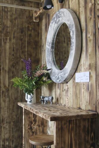 a mirror on a wooden wall with a table with flowers at The Moo-tel at Moody Meadows in Aberaeron