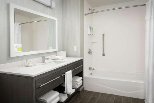 a bathroom with a sink and a tub and a mirror at Home2 Suites By Hilton Charlottesville Downtown in Charlottesville