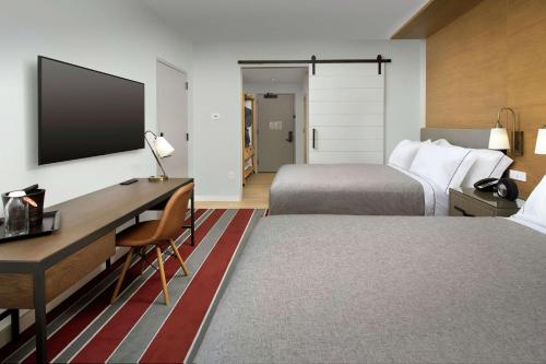 a hotel room with two beds and a desk and a tv at Canopy By Hilton Ithaca Downtown in Ithaca