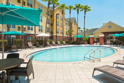 una piscina con mesas de sillas y sombrillas en un hotel en Homewood Suites by Hilton Orlando-UCF Area, en Orlando