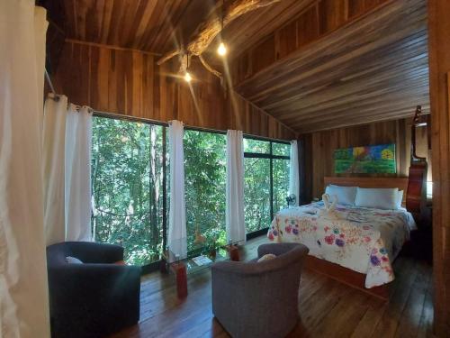 a bedroom with a bed and two chairs and windows at Jungle Living Tree Houses in Monteverde Costa Rica