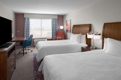 a hotel room with two beds and a desk and a television at Hilton Garden Inn - Salt Lake City Airport in Salt Lake City