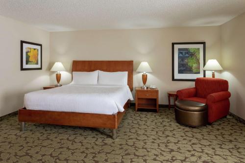 a hotel room with a bed and a red chair at Hilton Garden Inn St. Paul Oakdale in Oakdale