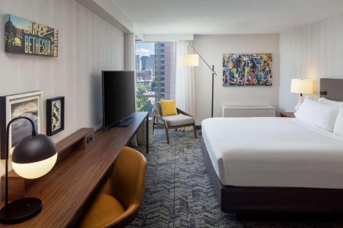 ベセスダにあるThe Bethesdan Hotel, Tapestry Collection by Hiltonのベッド、デスク、テレビが備わるホテルルームです。
