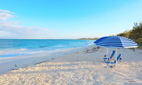 a blue and white umbrella and chairs on a beach at YellowBird home in South Palmetto Point
