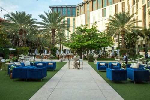 a courtyard with blue couches and tables and palm trees at Hilton West Palm Beach in West Palm Beach