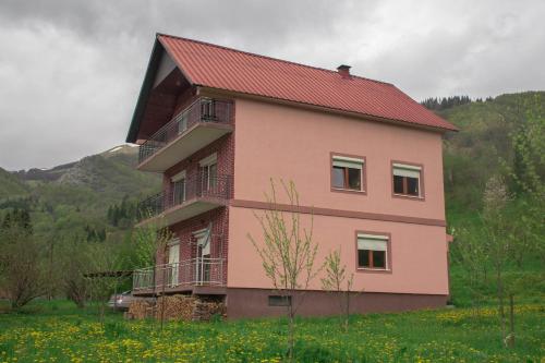 a pink house with a red roof in a field at Raj na selu - Padaberi paradise in Berane
