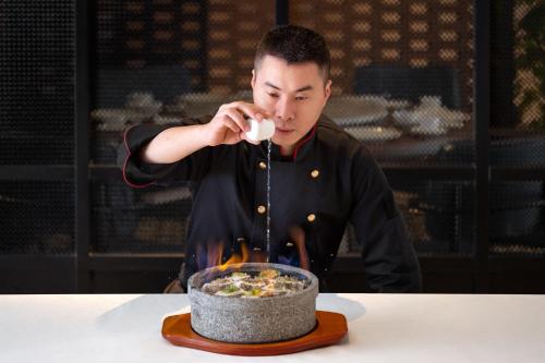 a man cooking a bowl of food on a table at Four Points by Sheraton Chongqing, Yongchuan in Yongchuan