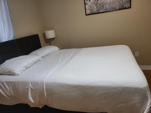 uma cama com lençóis brancos e almofadas num quarto em Lovely Place em Kingston