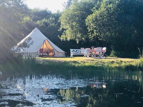 a tent with a table and a bench next to a lake at Rose in St Austell