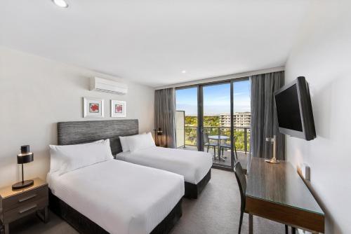 a hotel room with two beds and a desk at Adina Serviced Apartments Canberra Dickson in Canberra