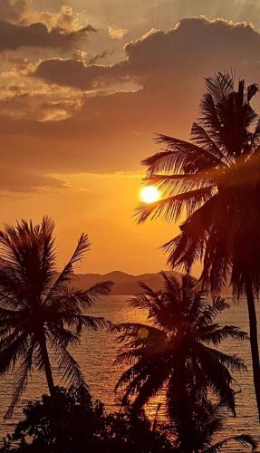 a sunset with palm trees in front of the ocean at Hillhouse - Koh Yao Noi in Ko Yao Noi