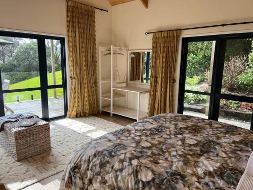 a bedroom with a large bed and large windows at Kākā Ridge Retreat Luxury Cottage in Tawharanui