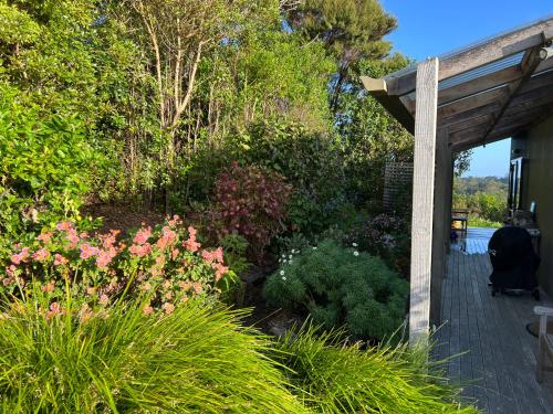 a garden with pink flowers and a wooden porch at Kākā Ridge Retreat Luxury Cottage in Tawharanui