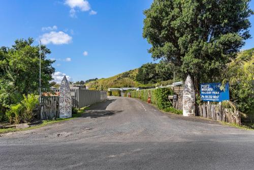 a road with a fence and a sign on a hill at Port Waikato Holiday Park in Port Waikato